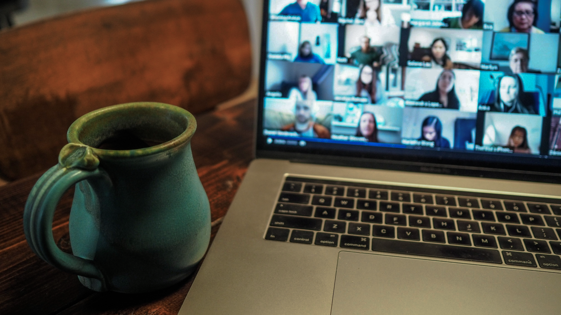 Coffe mug on a table with a laptop in a video meeting with a scrfeen full of people